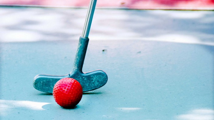 Roter Minigolf-Ball hinter dem ein Schläger zu sehen ist