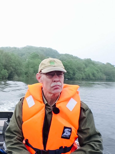 Johannes Pantel und Michael Knappstein im Motorboot im Wasser, einer am Lenkrad, der andere sitzt daneben, beide tragen orange Rettungswesten.