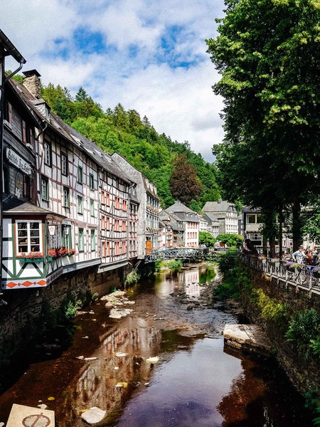 Links Fachwerkhäuser und ein Flusslauf. Rechts ein Dorfplatz, im Hintergrund weitere Fachwerkhäuser.