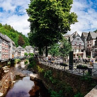 Links Fachwerkhäuser und ein Flusslauf. Rechts ein Dorfplatz, im Hintergrund weitere Fachwerkhäuser.