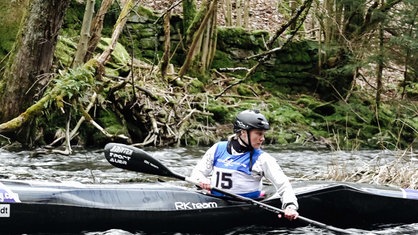 Eine Frau sitzt in einem Kanu auf einem Fluss und schaut sich um. Im Hintergrund Wald.