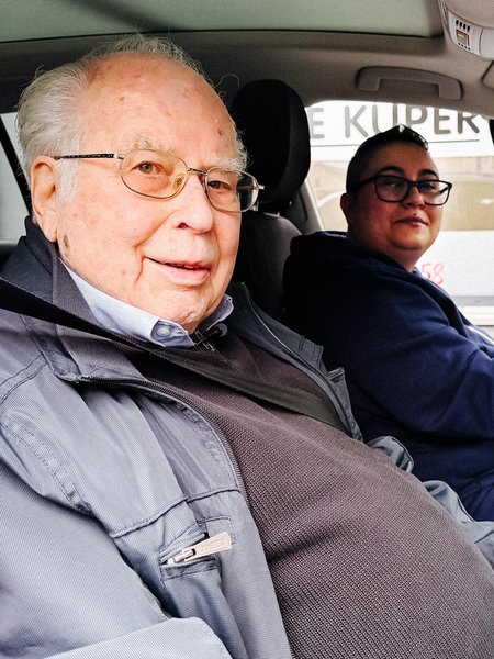 Wolfgang Küper sitzt neben seiner Schülerin im Fahrschulauto mit offenen Türen. Beide schauen in die Kamera.