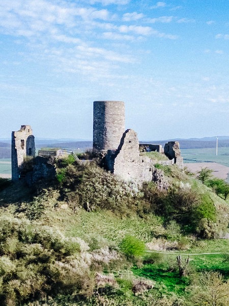 Auf dem Desenberg stehen der Turm und Mauern einer alten Burg, im Hintergrund Felder und Windräder