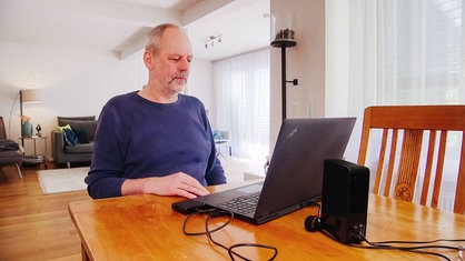 Ein Mann sitzt zuhause im Wohnzimmer mit Laptop am Schreibtisch.