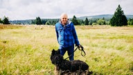 Schäfer Peter Kuhlmann steht mit seinem Hund auf der Hochheide. Im Hintergrund sind seine Schafe.