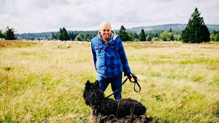 Schäfer Peter Kuhlmann steht mit seinem Hund auf der Hochheide. Im Hintergrund sind seine Schafe.