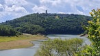Ausblick im Nationalpark Eifel auf einen bewaldeten Hügel mit der Burg Vogelsang und dem Urftsee