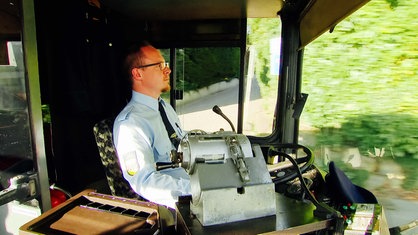 Ein Mann sitzt in einem Bus auf dem Fahrersitz und hat die Hände am Lenkrad