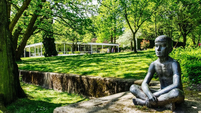 Eine Skulptur eines sitzenden Mannes in einem Stadtpark.