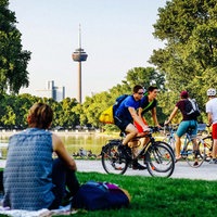 Menschen picknicken auf einer Wiese, im Hintergrund der Kölner Fernsehturm.