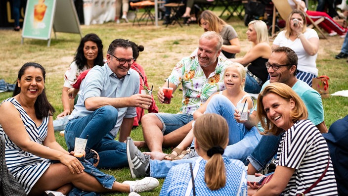 Ein Gruppe von Menschen sitzt auf einer Wiese und trinkt Cocktails.