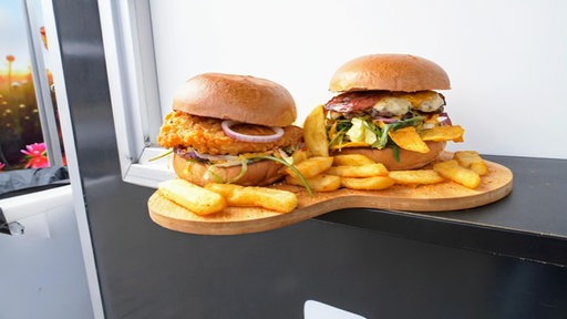 Nahaufnahme von zwei Burgern und Pommes auf einem Holztablett.