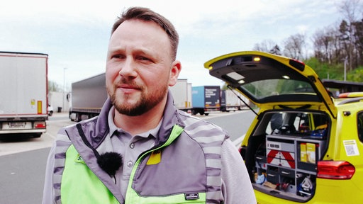 ADAC-Pannenhelfer Stefan Sonnemann steht auf einem Autobahn-Rastplatz.