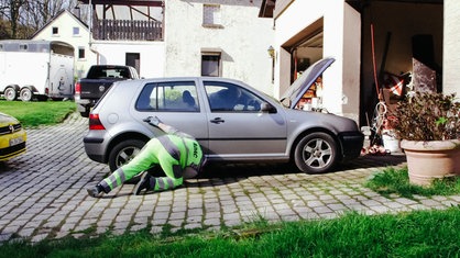 ADAC-Pannenhelfer Stefan Sonnemann hockt neben einem grauen Kleinwagen und klopft von unten mit einem Hammer gegen den Tank
