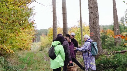 Mykologin Elena Newerdowski (rechts) steht vor fünf Personen. Sie hat ihre Hände ausgestreckt, auf denen Pilze liegen.