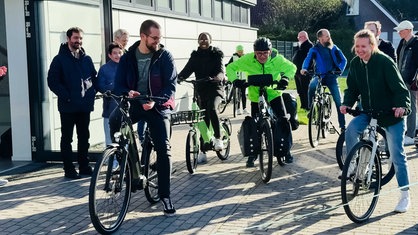 Einige Menschen stehen um Rainer Stephan in gelb-grüner Jacke und Helm auf einem Fahrrad, manche selbst auf einem Rad