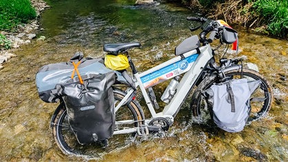 Das Fahrrad von Rainer Stephan ist mit einigen Taschen bepackt und steht in einem kleinen Fluss