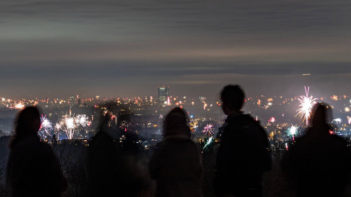 Menschen stehen auf dem nächtlichen Rodderberg und blicken auf das Feuerwerk