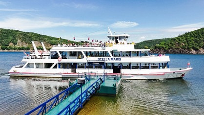 Ein weißes Passagierschiff mit der Aufschrift "Stella Maris" legt von einem Anleger auf einem See ab.