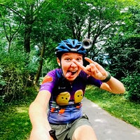 Eine junge Frau mit Helm fährt schnell auf einem Longboard, sie lacht in die Kamera und streckt die Zunge raus