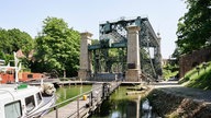 Schiffshebewerk in Henrichenburg über einem Fluss, mit vier Türmen an den Ecken. Im Vordergrund Boote.