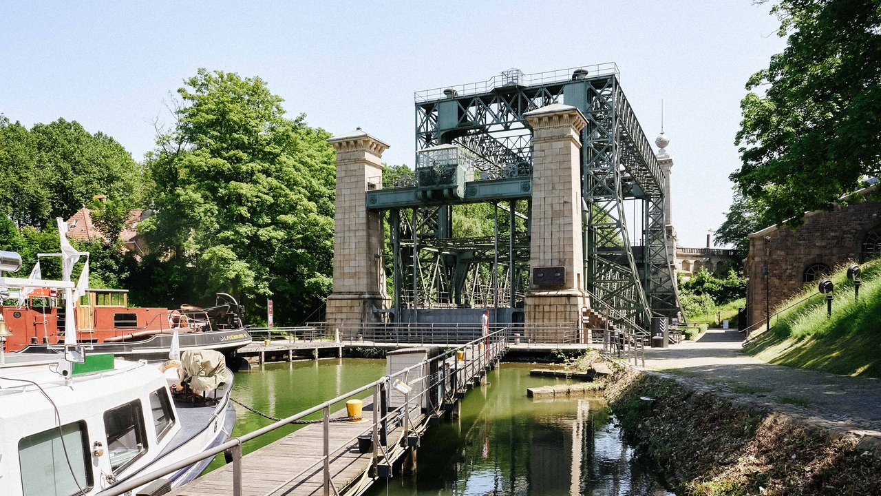 Schiffshebewerk in Henrichenburg über einem Fluss, mit vier Türmen an den Ecken. Im Vordergrund Boote.