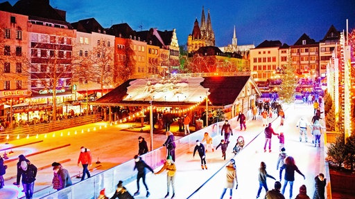 Menschen laufen auf der illuminierten Eisbahn auf dem Heumarkt in Köln am Abend Schlittschuh.