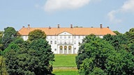 Schloss Cappenberg mit rotem Dach und weißer Fassade. Im Hintergrund Wald und Felder.
