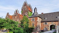 Schloss Heessen. Das Gebäude besteht aus roten Ziegeln, teilweise mit Pflanzen bedeckt.