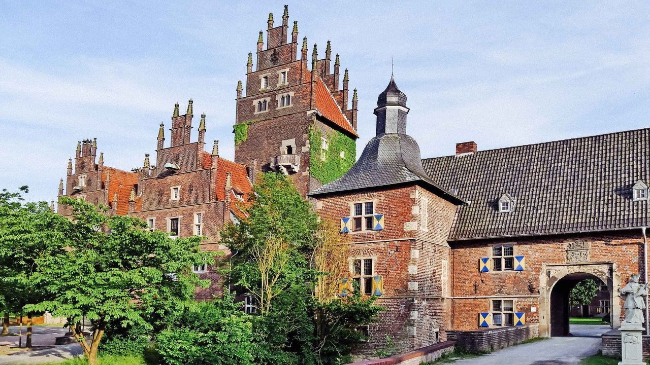 Schloss Heessen. Das Gebäude besteht aus roten Ziegeln, teilweise mit Pflanzen bedeckt.