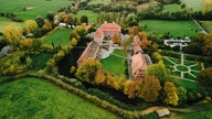 Schlossanlage Oberwerries mit roten Dächern. Rundherum Bäume.
