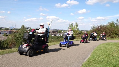 Mitglieder der Duisburger Scootergang fahren auf ihren Elektromobilen einen Weg hinauf.