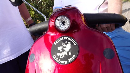 Auf der Vorderseite eines roten Elektromobils prangt das schwarz-weiße Logo der Scootergang.