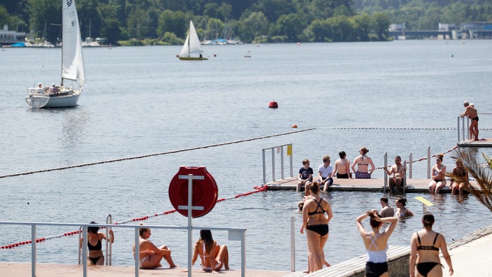 Mehrere Badegäste schwimmen und sitzen an der Badestelle am Essener Baldeneysee.