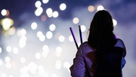 Eine Frau betrachtet vor einem dunklen Hintergrund ein Feuerwerk, sie ist nur von hinten zu sehen