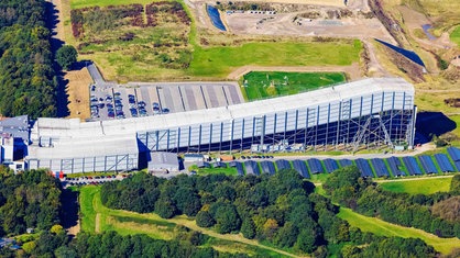 Luftaufnahme einer großen Skihalle mit langer Skipiste, inmitten von Grünflächen.