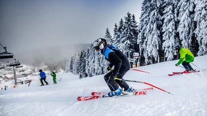 Skifahrer fahren in Winterberg eine schneebedeckte Piste hinunter.