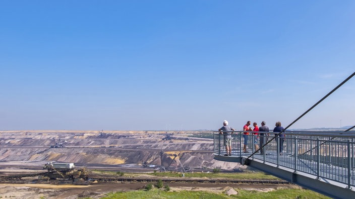 Fünf Menschen blicken von der Aussichtsplattform in das große Loch des Tagebaus Garzweiler.
