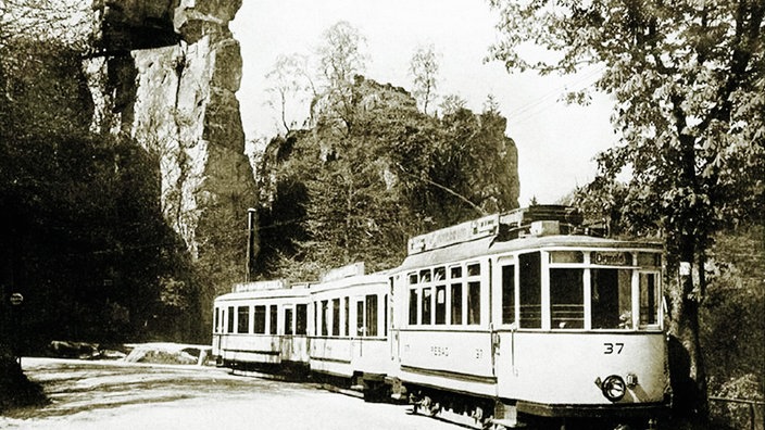 Ein altes Bild einer Straßenbahn, die zwischen den Externsteinen hindurch fährt.
