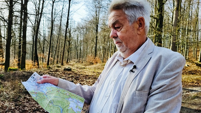Werner Zahn in einem Wald. In der Hand hält er die Karte, die er von einem Bekannten erhalten hat. 