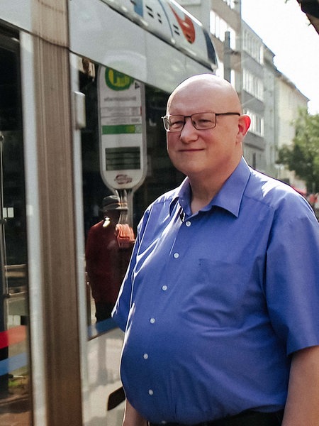 Ludwig Schönefeld steht vor einer Straßenbahn. Er lächelt.