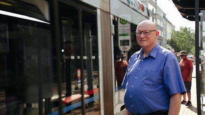 Ludwig Schönefeld steht vor einer Straßenbahn. Er lächelt.