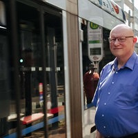 Ludwig Schönefeld steht vor einer Straßenbahn. Er lächelt.