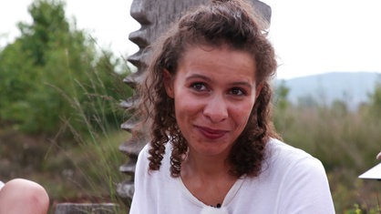 Sophie Brinkhoff, braunes, lockiges Haar, weißes T-Shirt, im Hintergrund grünes Gestrüpp