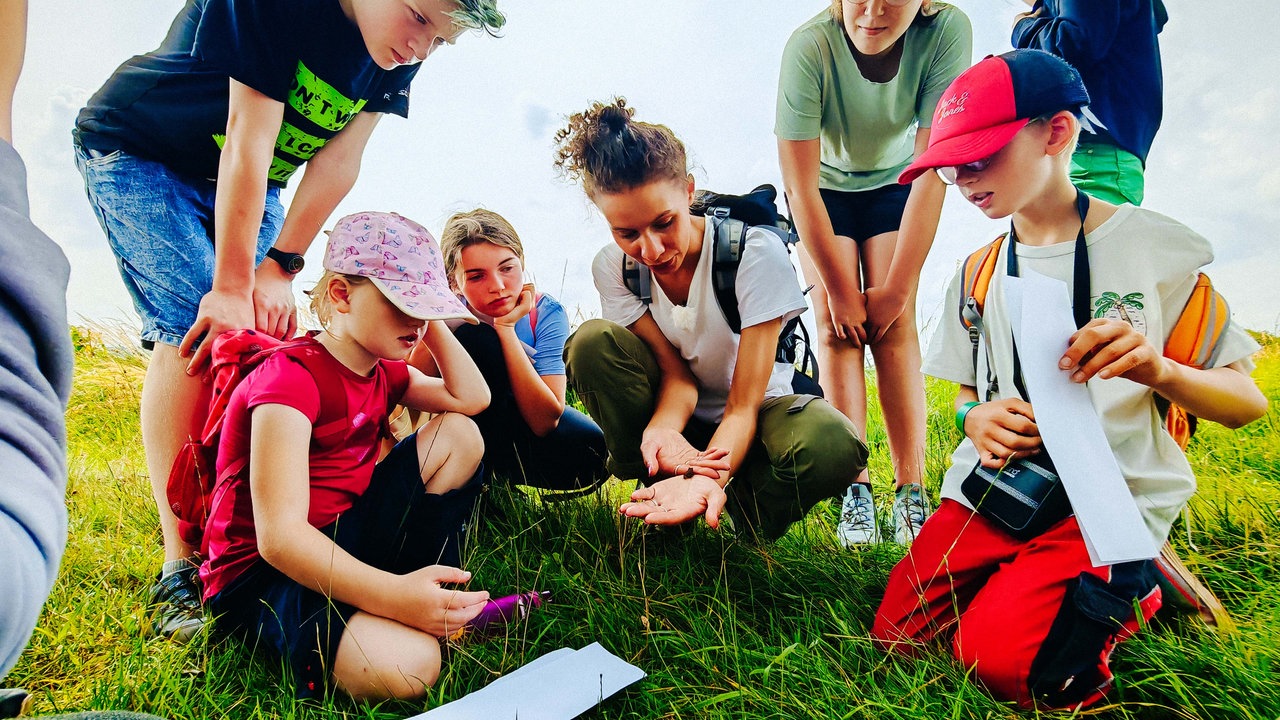 Sophie Brinkhoff in der Hocke, sie zeigt Kindern einen kleiner Frosch, der auf ihrer Hand sitzt.
