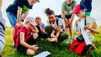 Sophie Brinkhoff in der Hocke, sie zeigt Kindern einen kleiner Frosch, der auf ihrer Hand sitzt.