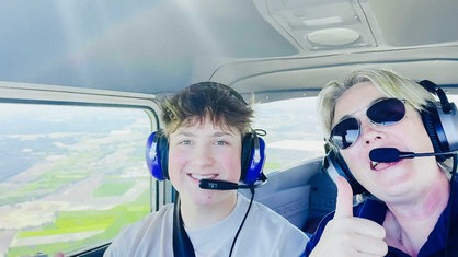 Ein Jugendlicher und eine Frau sitzen im Cockpit eines Flugzeugs und zeigen "Daumen hoch".