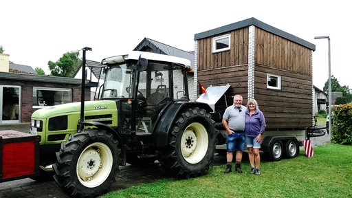Rentnerpaar Hubert und Franziska Meyer stehen vor einem Traktor. Auf dessen Anhänger steht ein Tinyhaus aus Holz.