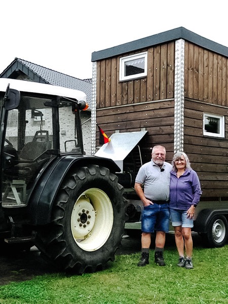 Rentnerpaar Hubert und Franziska Meyer stehen vor einem Traktor. Auf dessen Anhänger steht ein Tinyhaus aus Holz.
