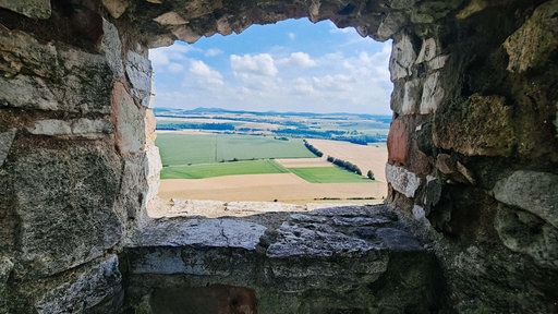 Die Aussicht aus der Steinmauer der Burgruine auf Felder und Hügel in der Ferne.